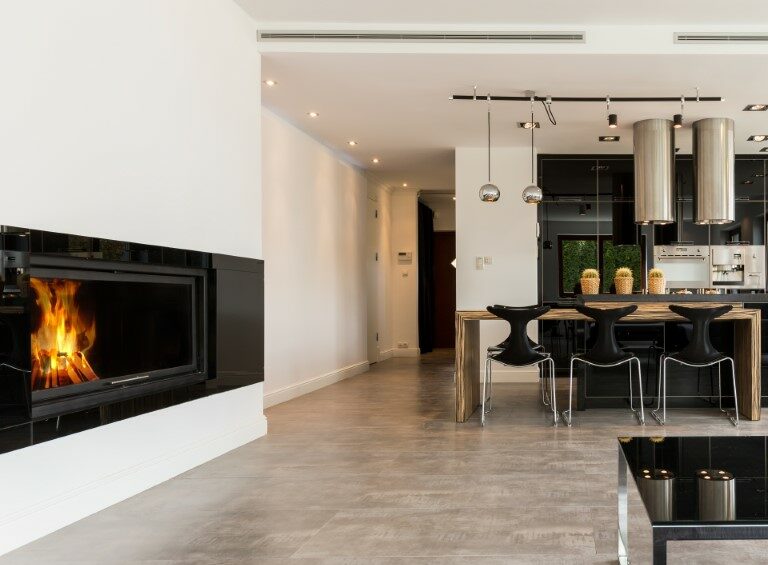 Spacious interior with fireplace, sofa, small table, dining set and black open kitchen